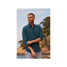 Homme avec chemise en lin bleu, col boutonné, décor naturel, style décontracté en bord de mer.