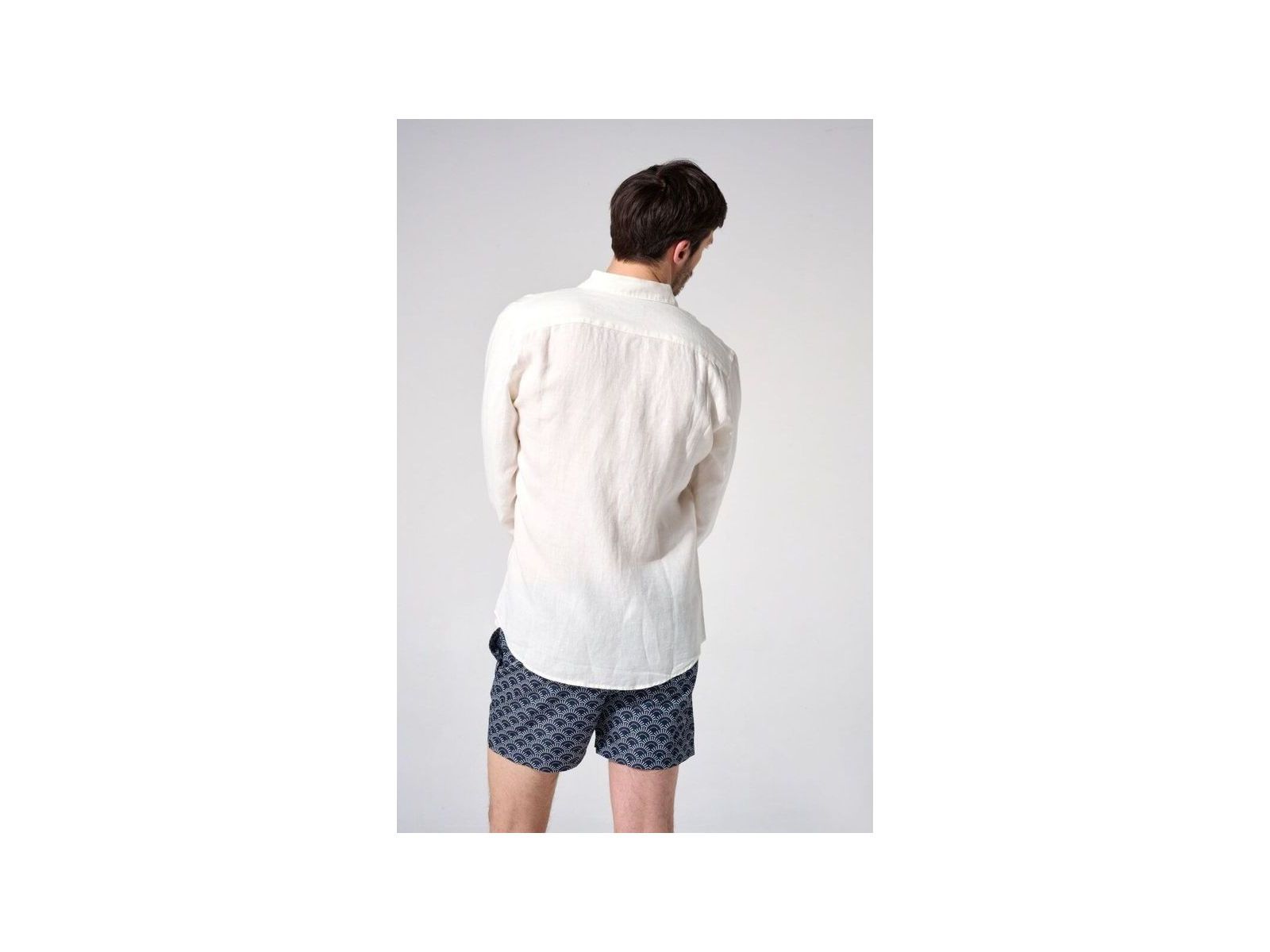 Homme portant une chemise en lin naturel européenne, vue de dos, avec des shorts à motifs, style décontracté.