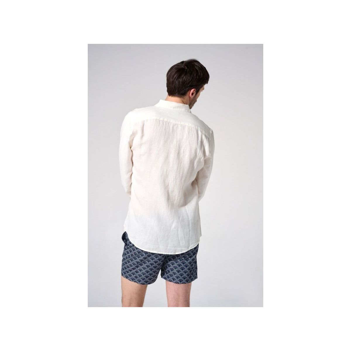 Homme portant une chemise en lin naturel européenne, vue de dos, avec des shorts à motifs, style décontracté.