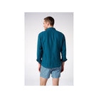 Homme portant une chemise en lin turquoise vue de dos, associée à des shorts imprimés.