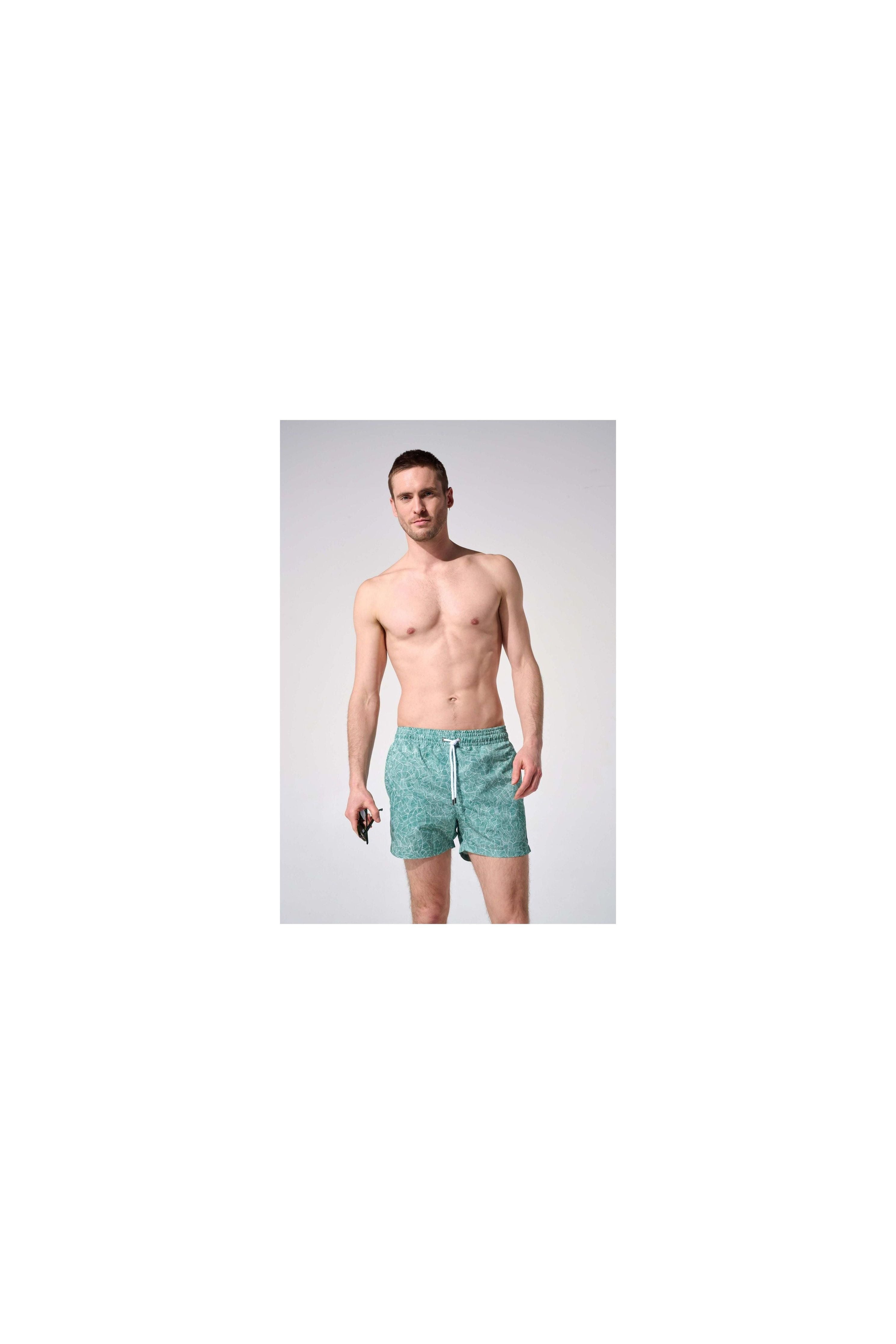 Homme portant des shorts de bain reflets, coupe ajustée, tissu recyclé, avec poches et ceinture élastique.