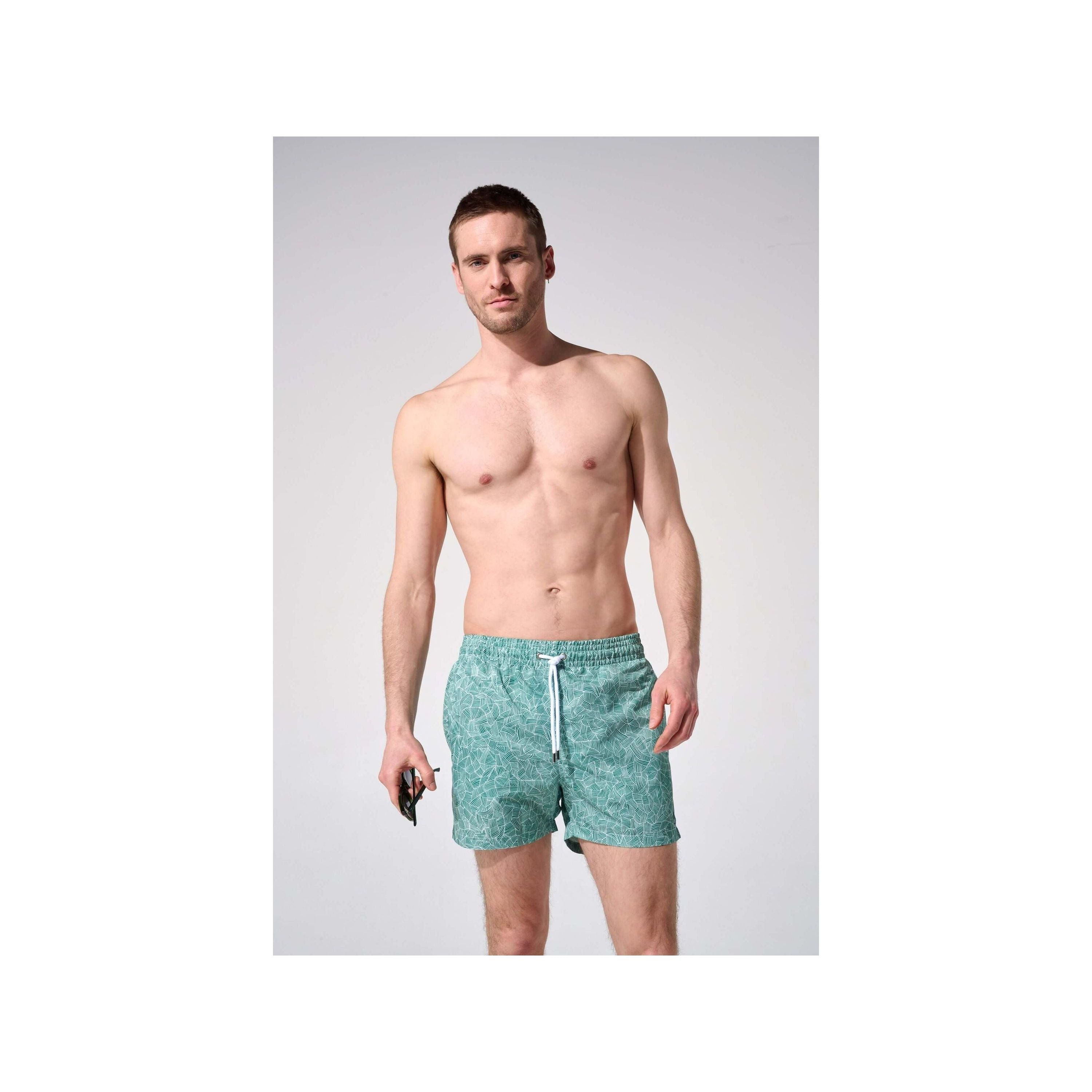 Homme portant des shorts de bain reflets, coupe ajustée, tissu recyclé, avec poches et ceinture élastique.