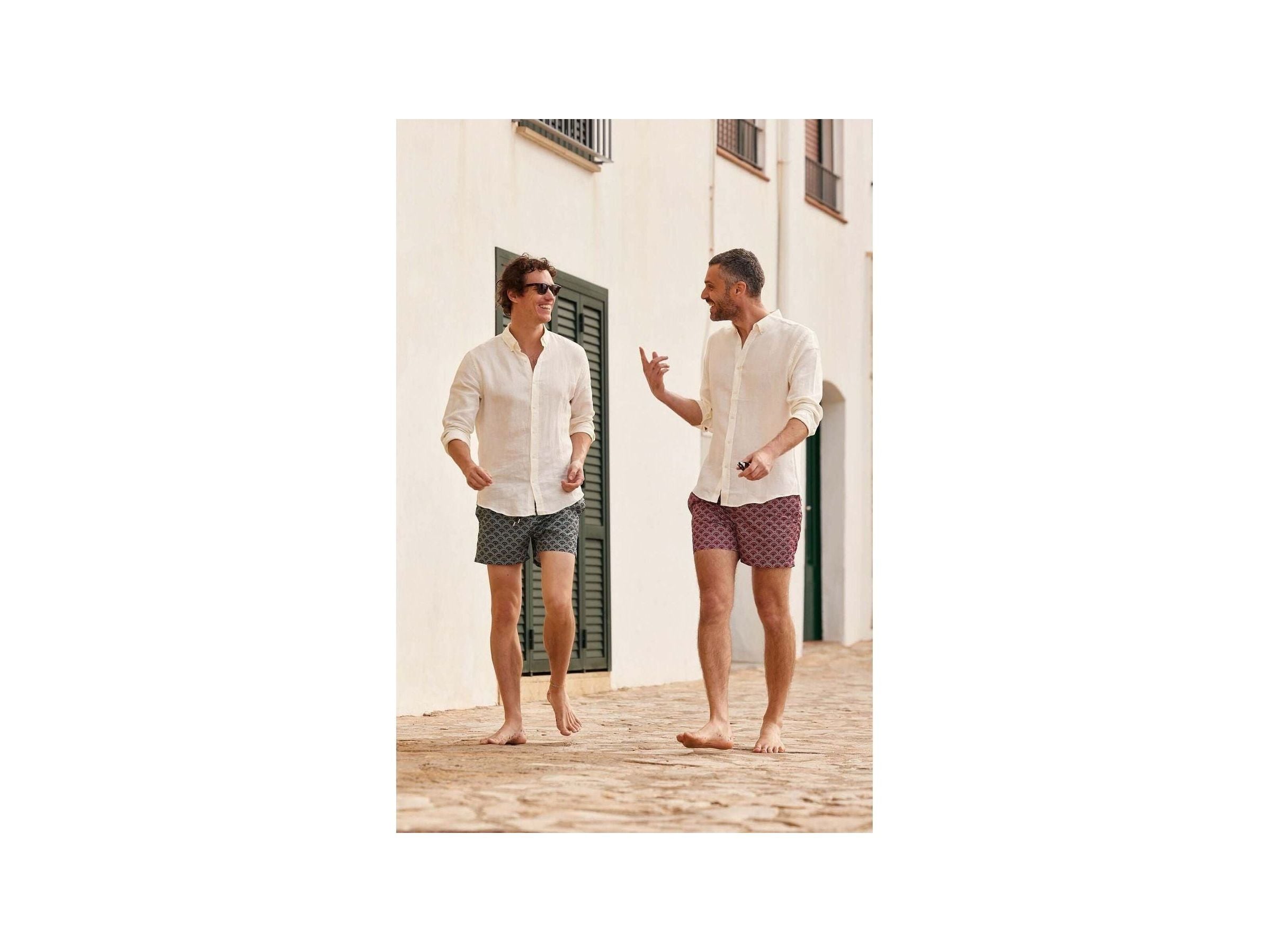 Two men wearing Ecume swim shorts, walking barefoot on a cobblestone path, enjoying a sunny day.