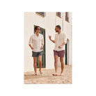 Two men wearing Ecume swim shorts, walking barefoot on a cobblestone path, enjoying a sunny day.