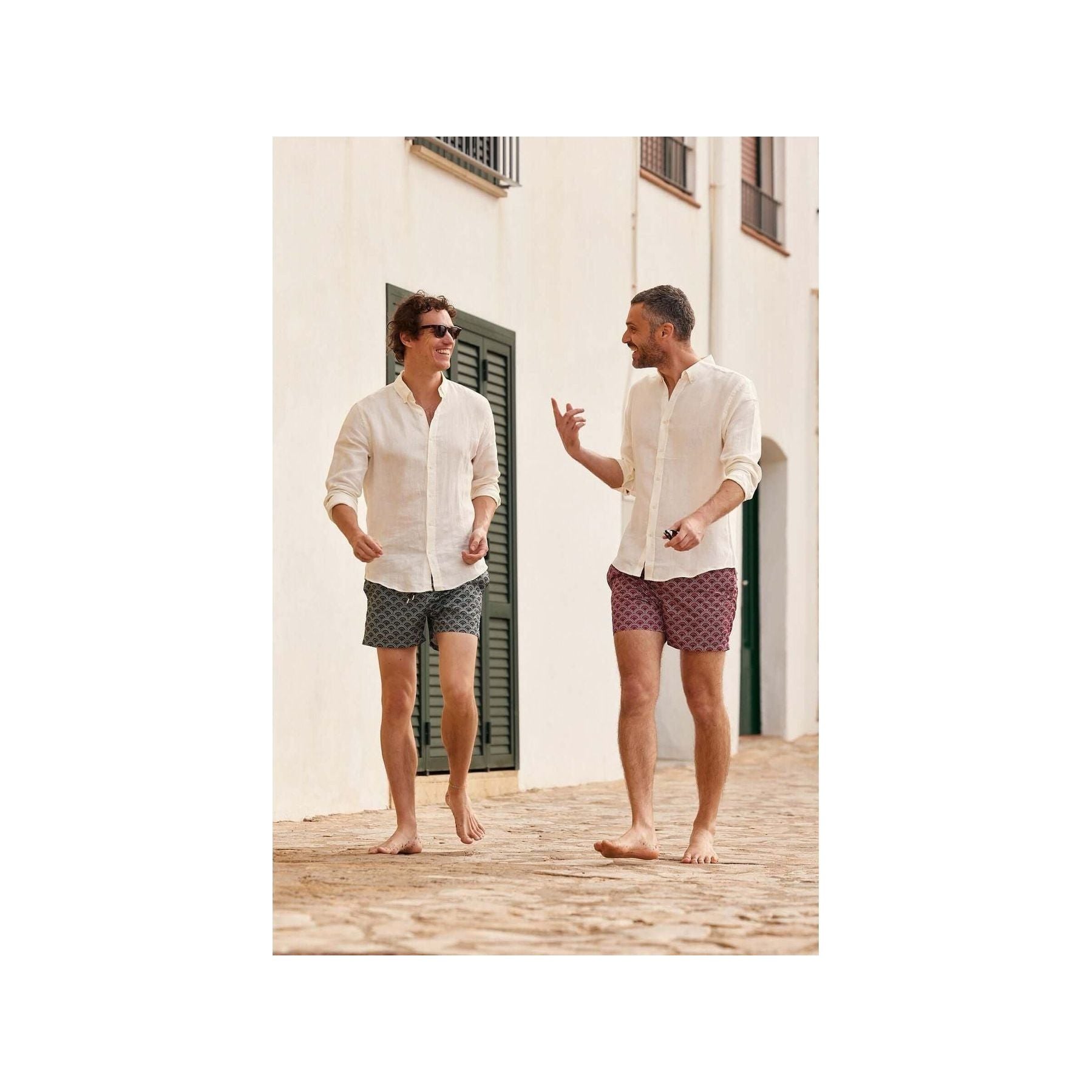 Two men wearing Ecume swim shorts, walking barefoot on a cobblestone path, enjoying a sunny day.